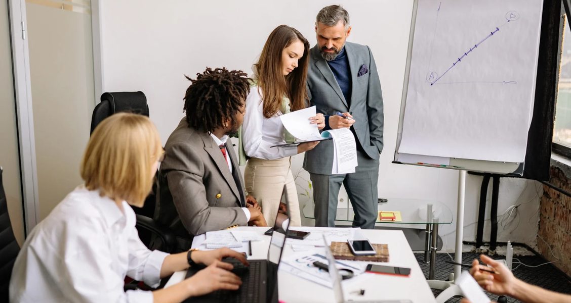 Sales team reviewing a proposal together beside a flip chart tracking deal progress