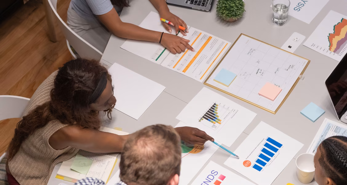 Sales team reviewing charts, deadlines, and a project calendar around an office table