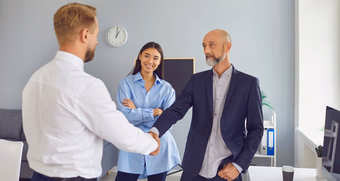 Manager shakes hands with a new hire as a colleague smiles, the moment a new employee announcement introduces