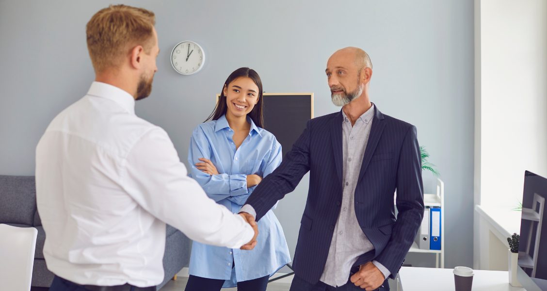 Manager shakes hands with a new hire as a colleague smiles, the moment a new employee announcement introduces