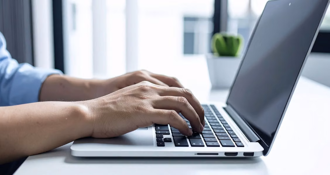Close-up of hands typing a client onboarding email on a laptop