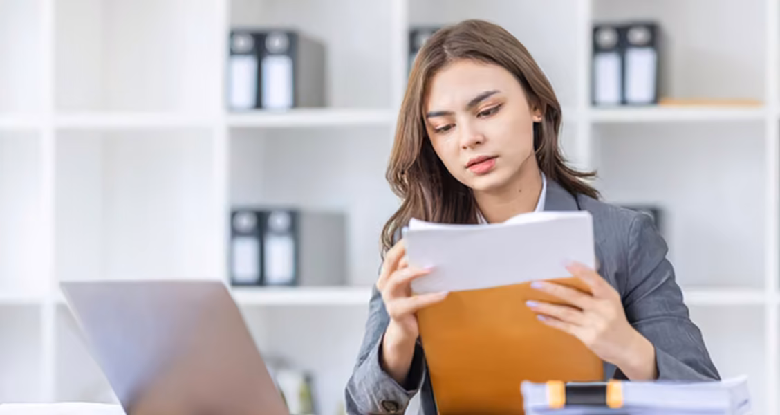 Professional reads a letter taken from an envelope at her desk, as a buyer reads an RFP cover letter