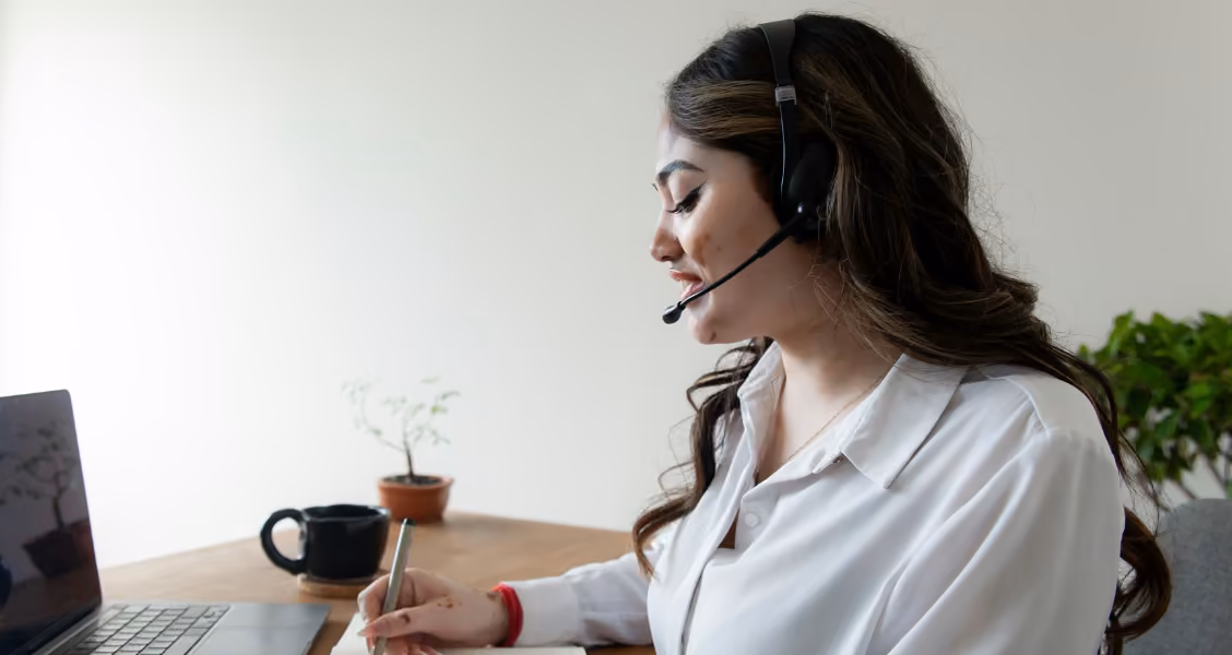 Sales rep wearing a headset takes notes during a call, where a sales battlecard keeps answers at hand