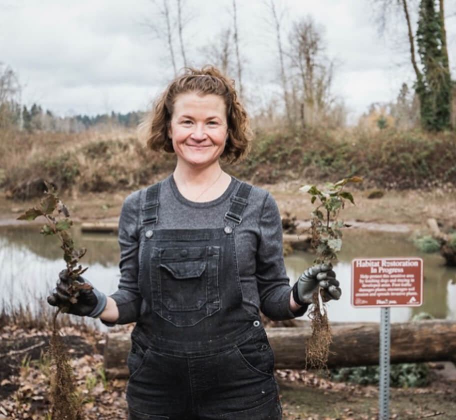 A woman standing in front of a lake holding two plants.