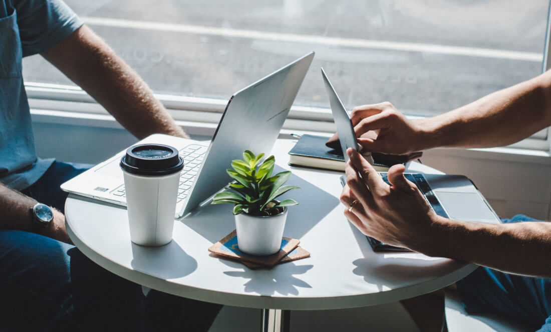 Two people with laptops sitting at a small, round table.