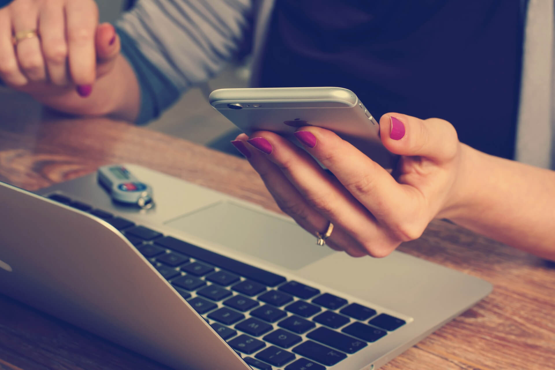 Hand holding a mobile phone with a laptop on desk.