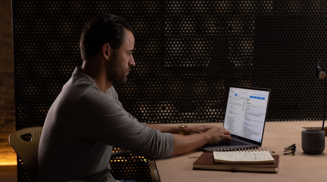 A man sitting at a desk, typing on a laptop.