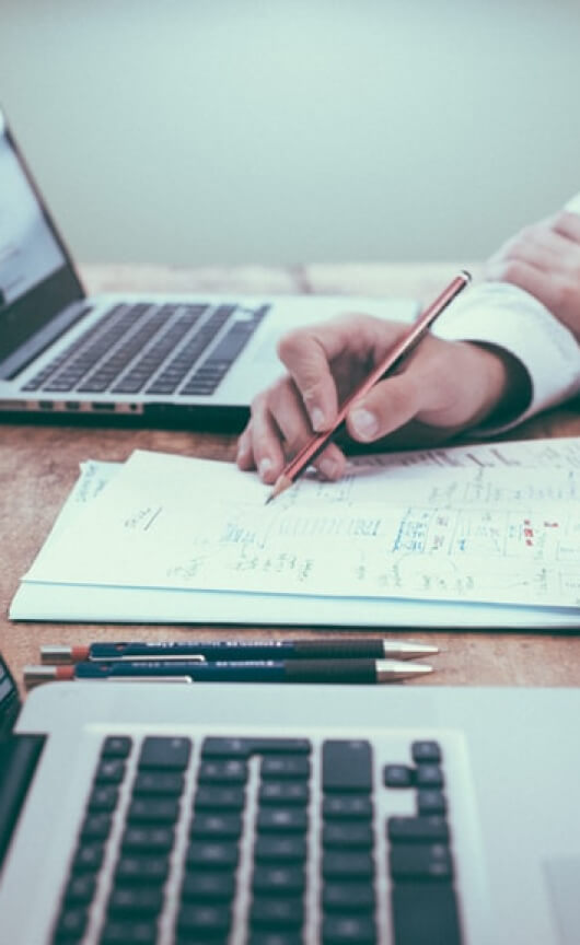 A hand making notes on paper with a laptop either side of the notepad.