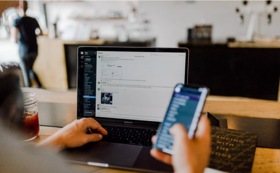 Person using a laptop with a mobile phone in hand