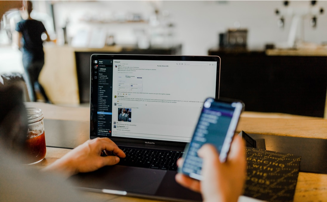 Person using a laptop with a mobile phone in hand