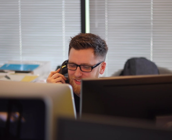 A man sitting at a desk talking on a telephone.