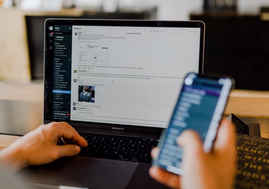 Person using a laptop with a mobile phone in hand.