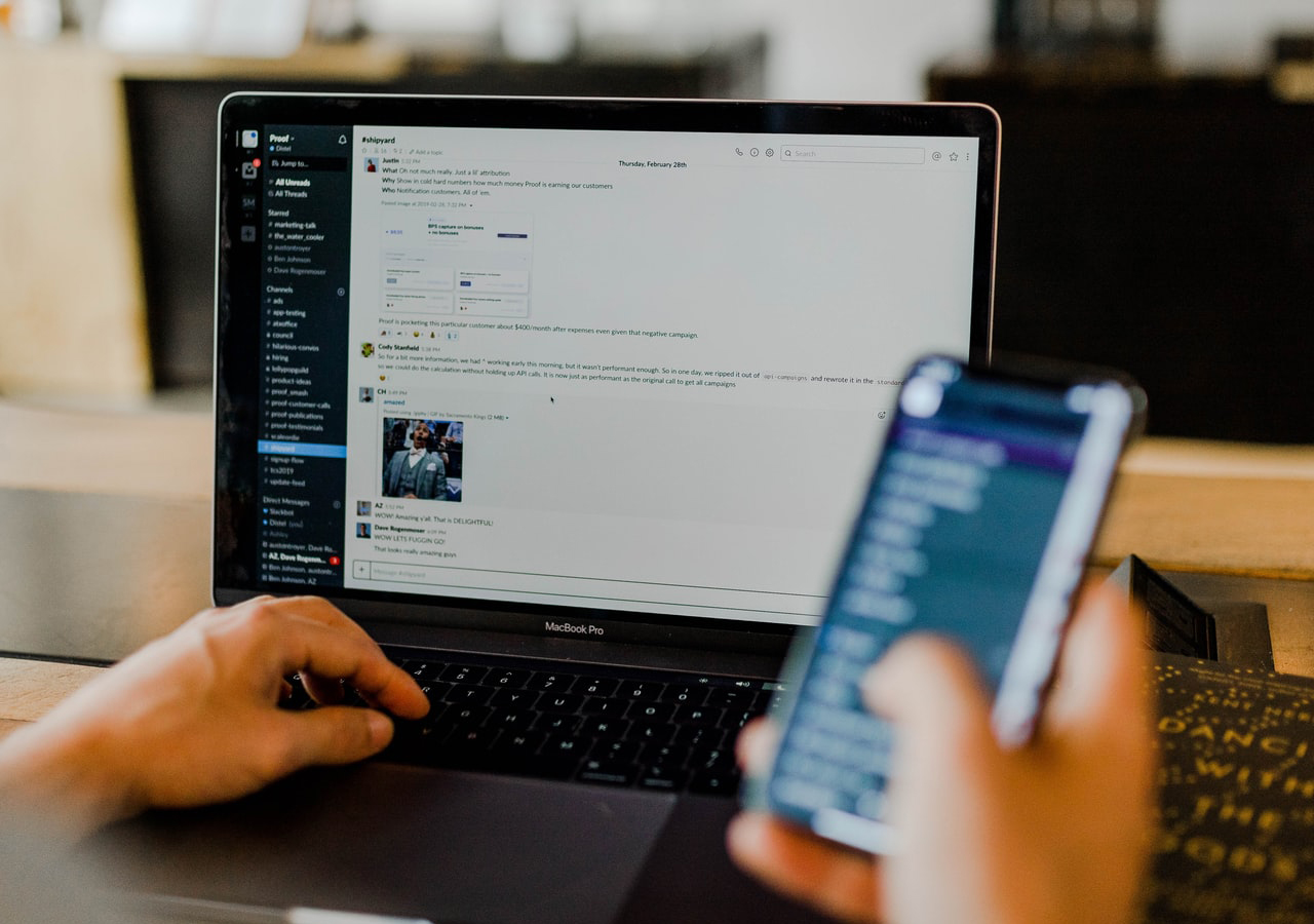 Person using a laptop with a mobile phone in hand.