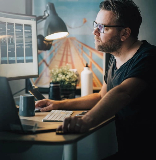 Man sitting at a desk looking at a monitor screen.