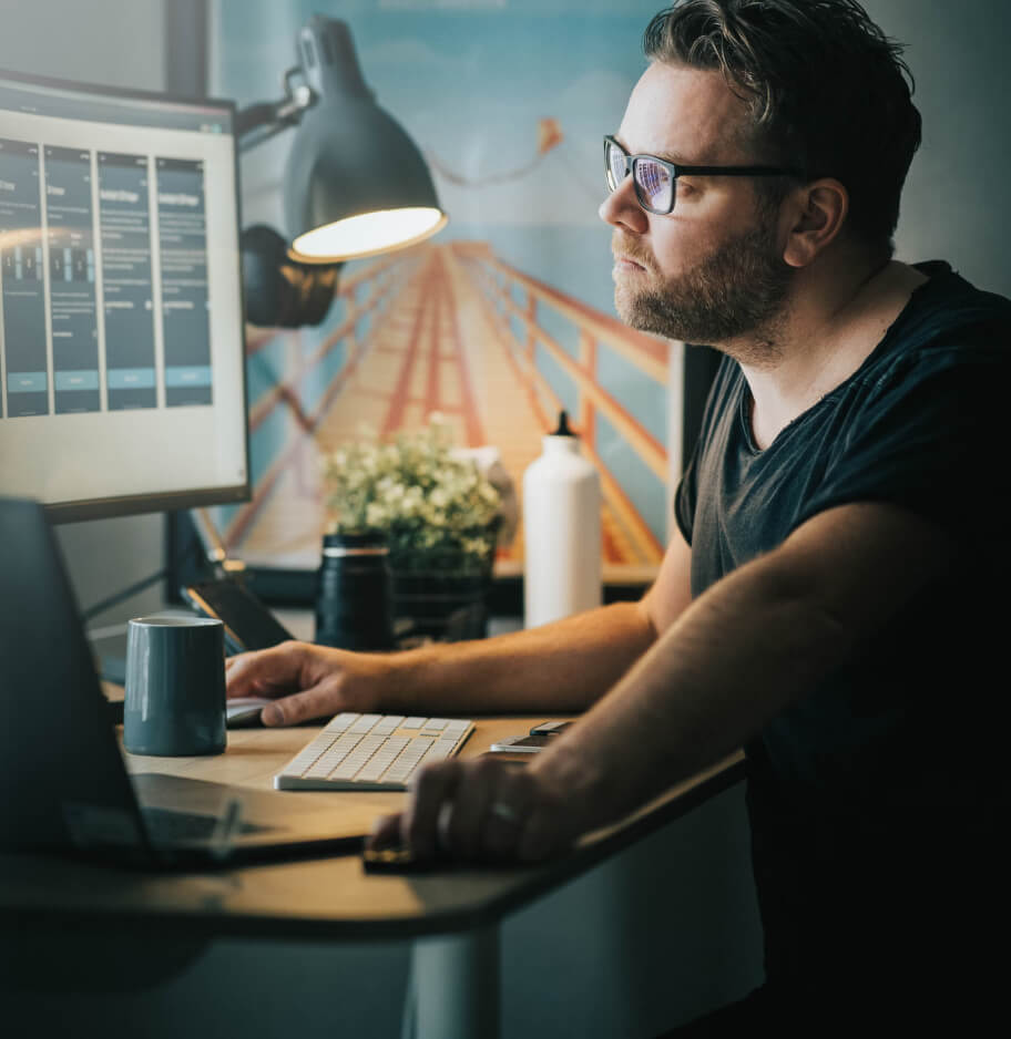 Man sitting at a desk looking at a monitor screen.
